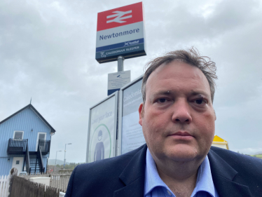 Jamie standing in front of the sign for Newtonmore Railway Station